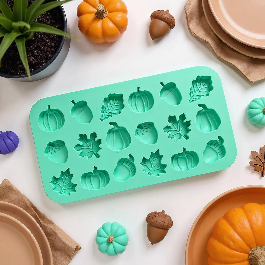 Silicone mold with pumpkin, leaf, and acorn shapes on a white surface with decorative items.